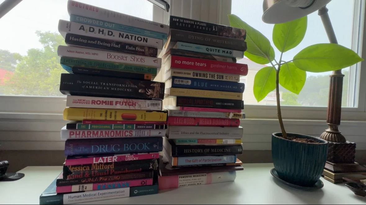 Stack of medical and science books on a desk near a window with green plants outside.